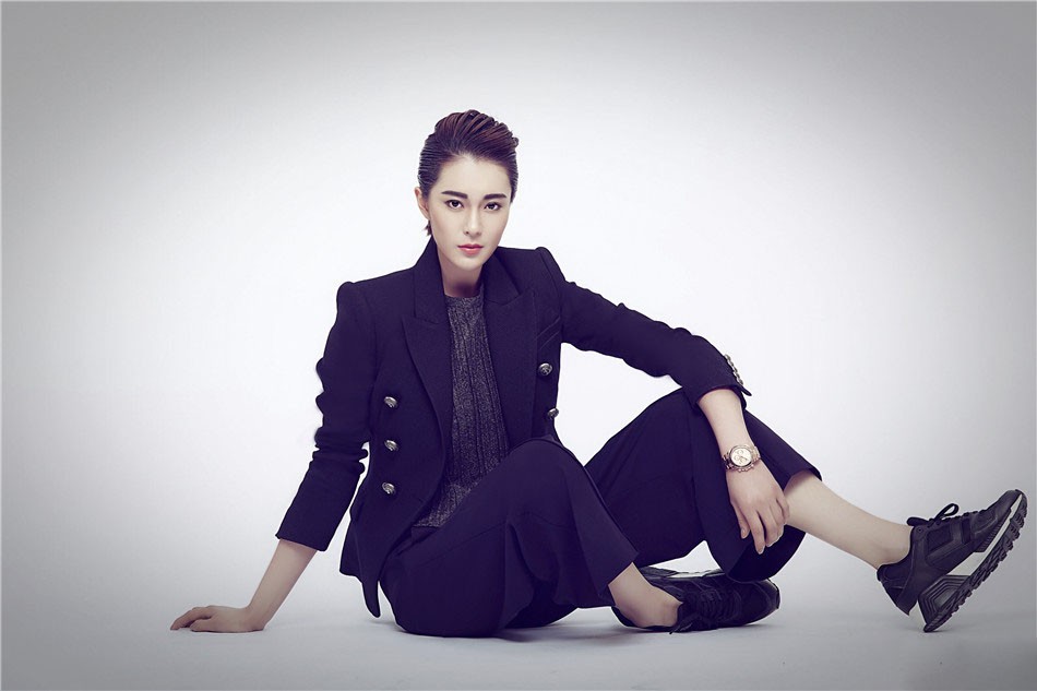 胡然身穿剪裁精良的灰色格纹套装，双手随意插袋立于光影交错处，尽显摩登复古与潇洒不羁的双重魅力