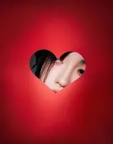 在爱心主题的光影背景下，鞠婧祎轻倚道具，小黑裙的质感与柔和的爱心光芒形成温柔与冷艳的独特碰撞，画面充满故事感