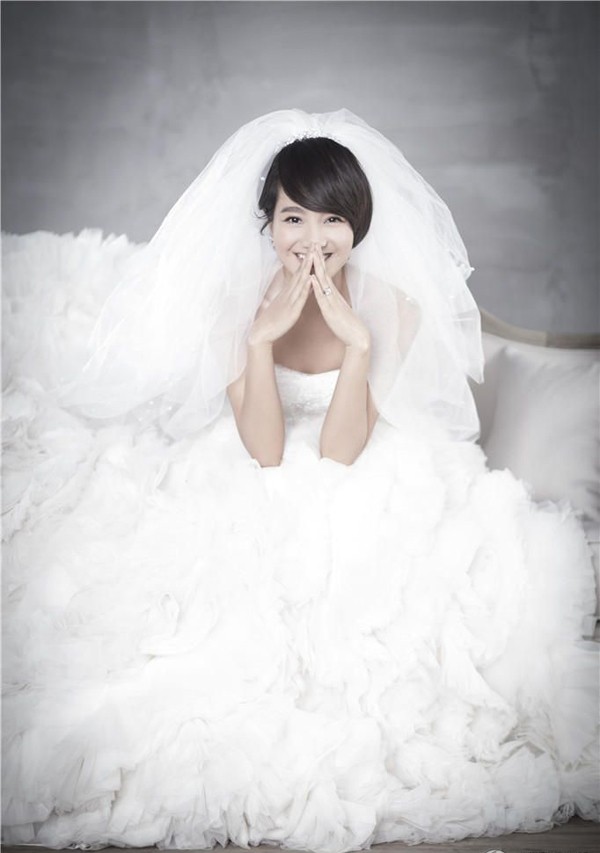 朱丹倚靠墙壁展露灿烂笑容，简约婚纱与纯粹笑容交织出极致清新感