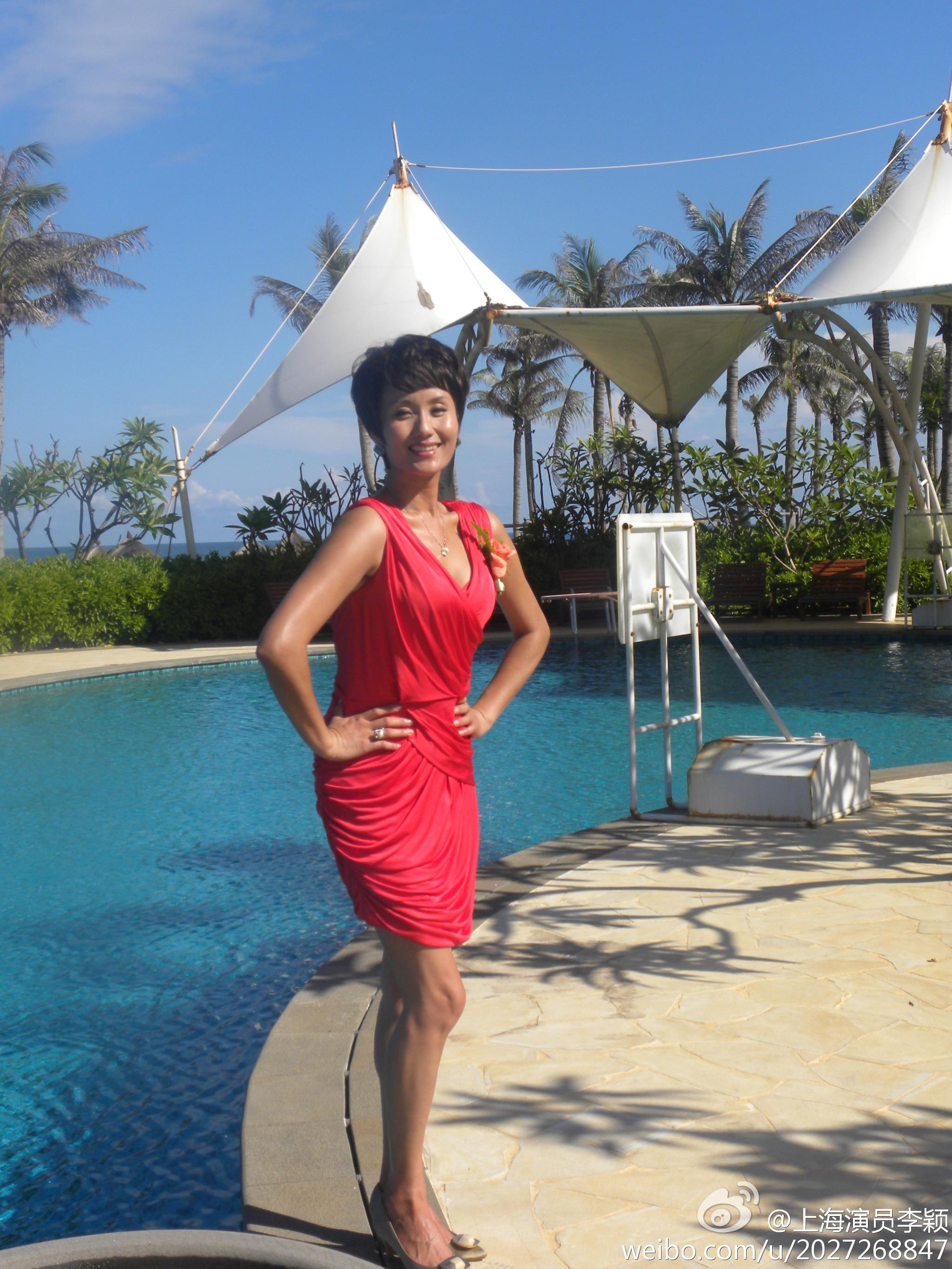 李颖优雅端坐，红色短裙下的修长美腿在丝袜衬托下更显线条，高跟鞋尖轻轻点地