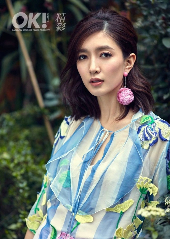 江疏影轻抚发丝倚坐于沙发，刺绣裙摆如花瀑般垂坠散落，在窗边光影中尽显动态柔美